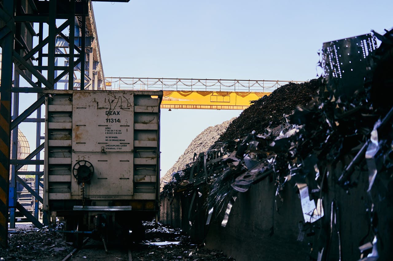 why-choose-us Train car at an industrial scrap metal yard with conveyor belt and metal piles.